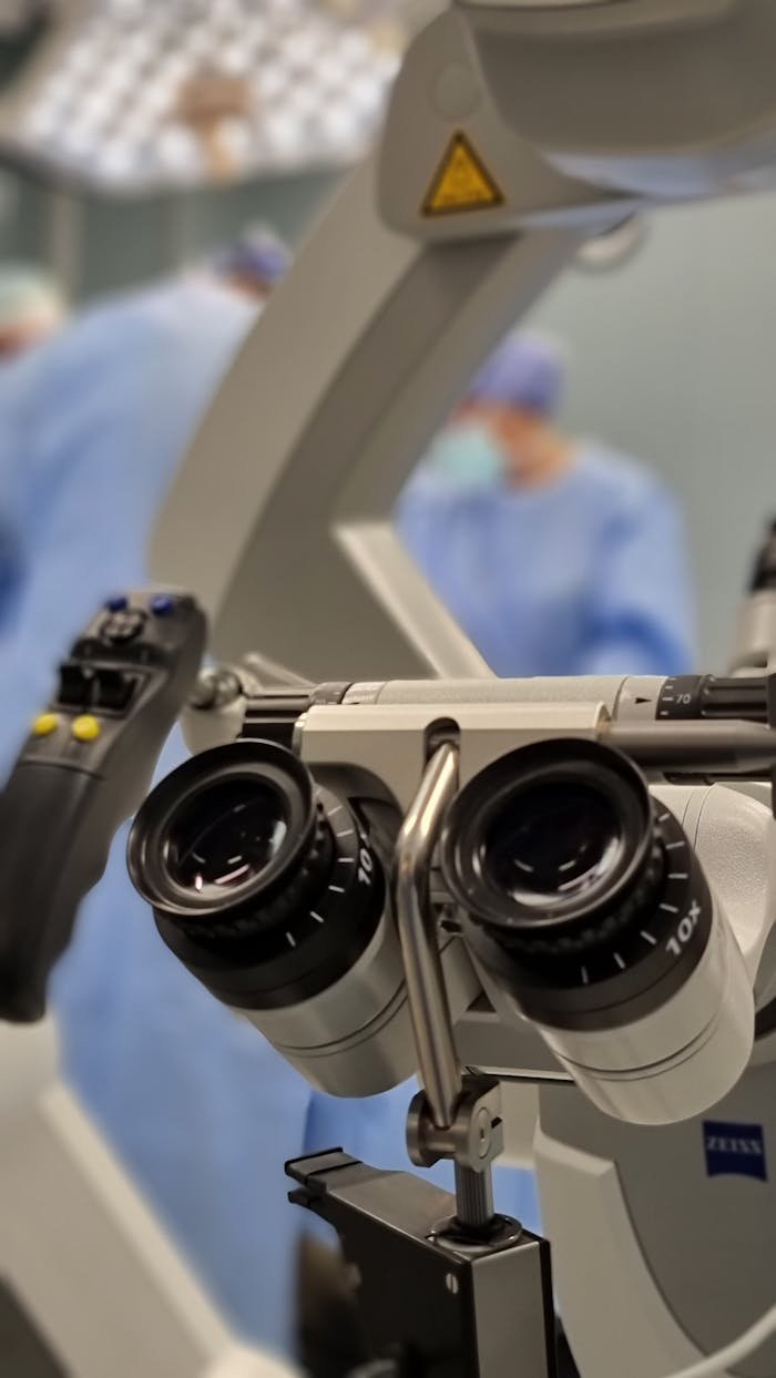 Close-up of a surgical microscope in an operating room setting with blurred medical team in background.